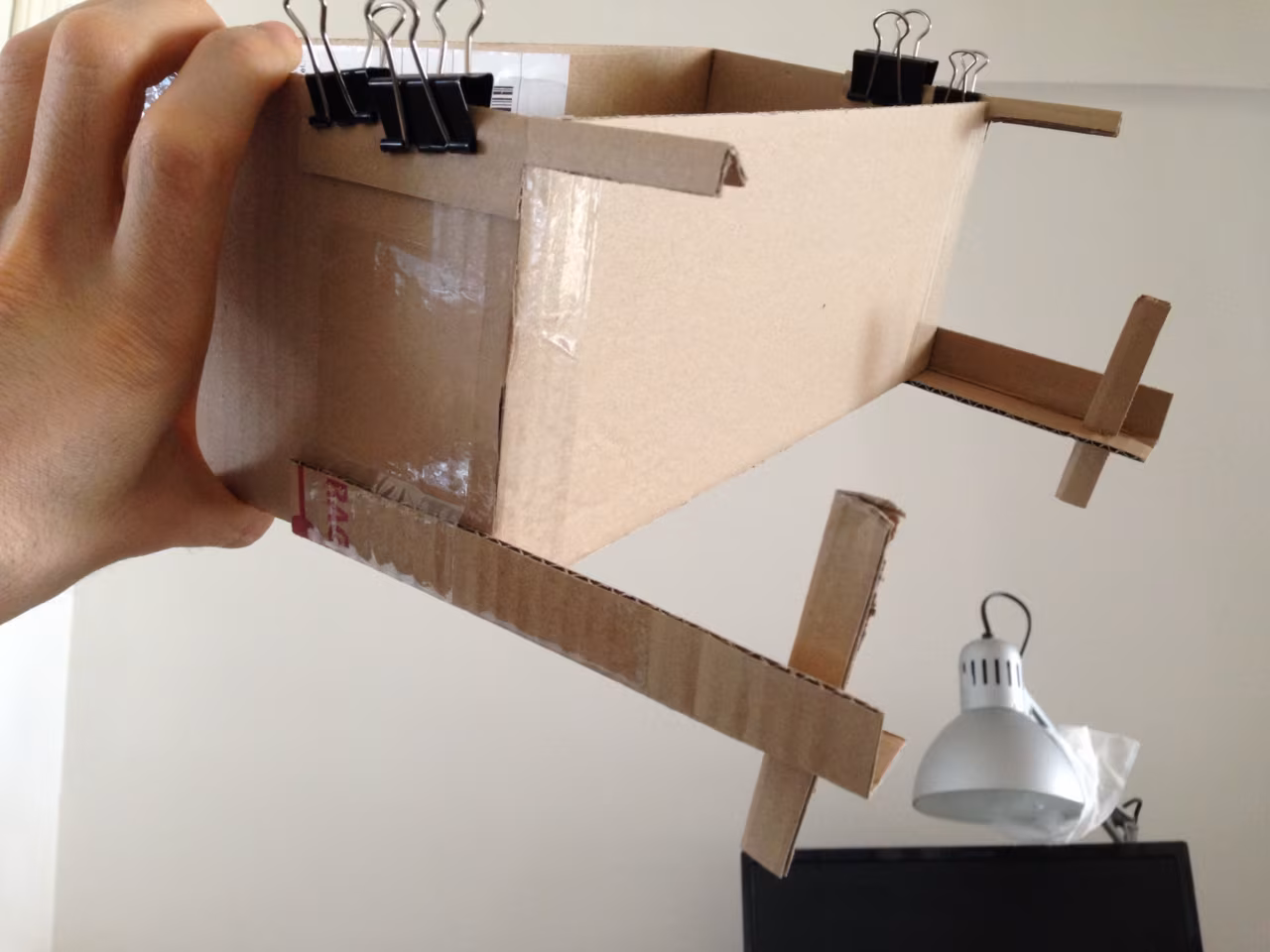 Cardboard prototype held by hand, with binder clips and wooden arms
