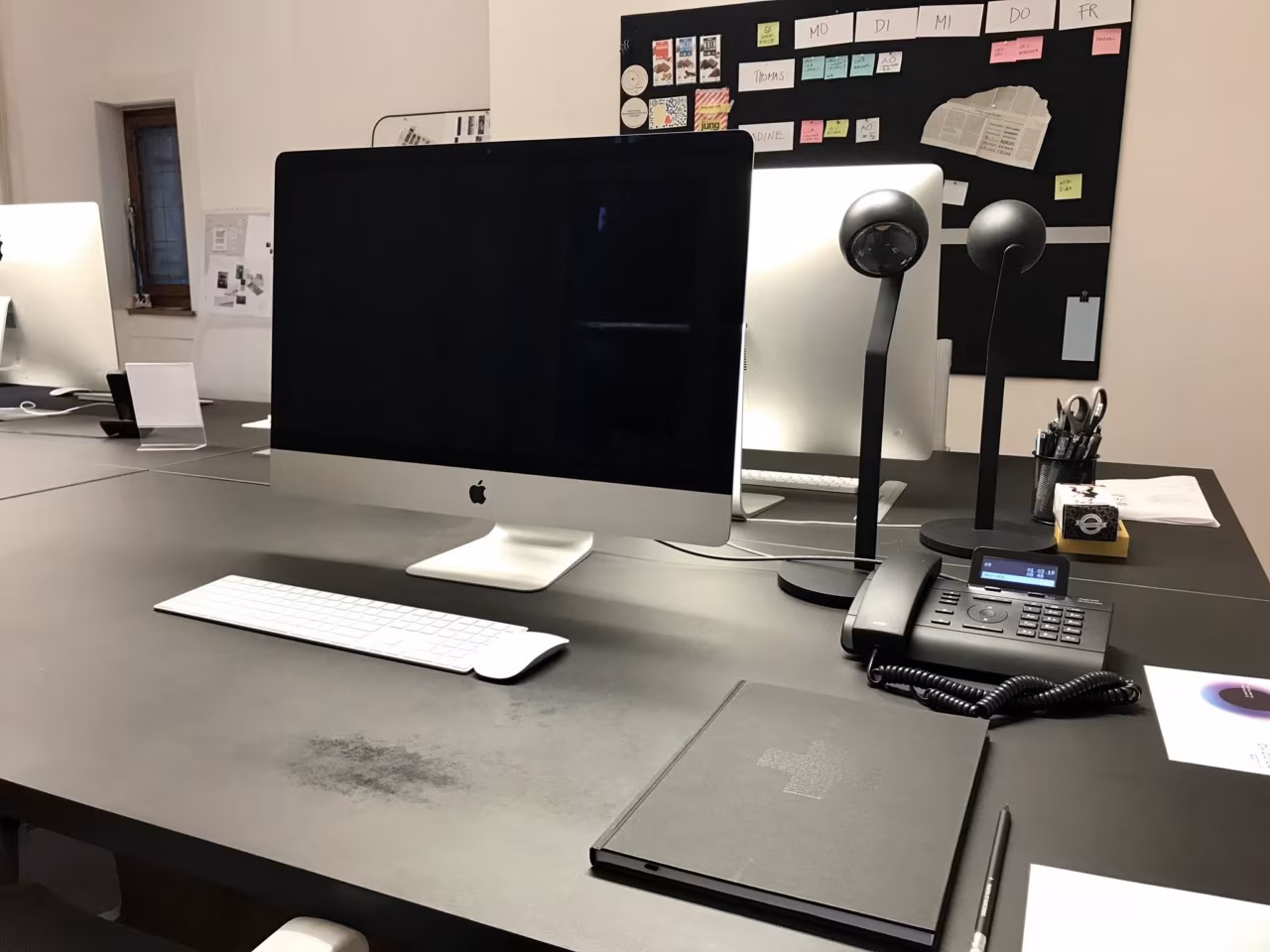 A workplace at Martin et Karczinski with an iMac, desk lamps and a moodboard wall