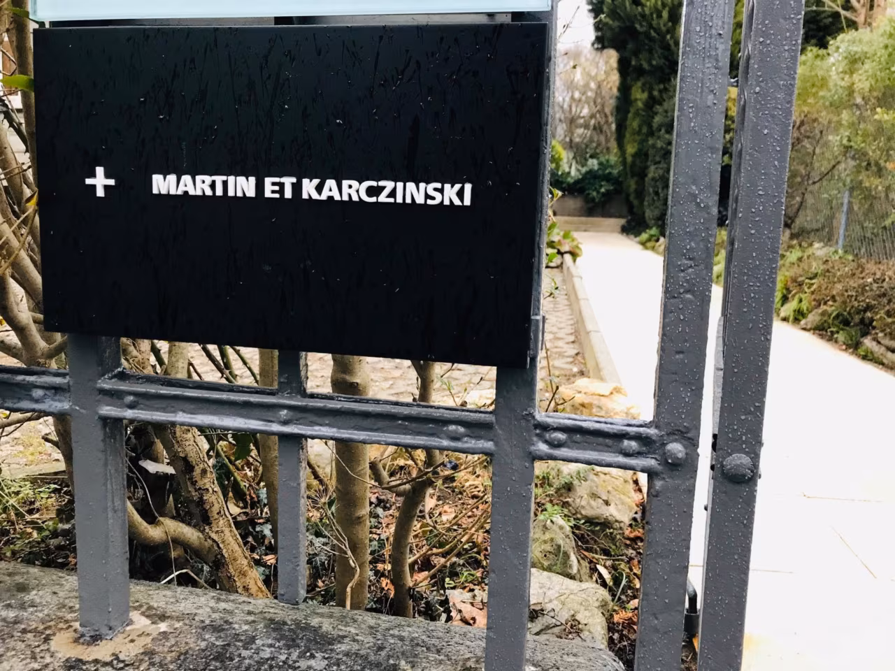 Black sign reading Martin et Karczinski at the garden gate of the agency in Zurich