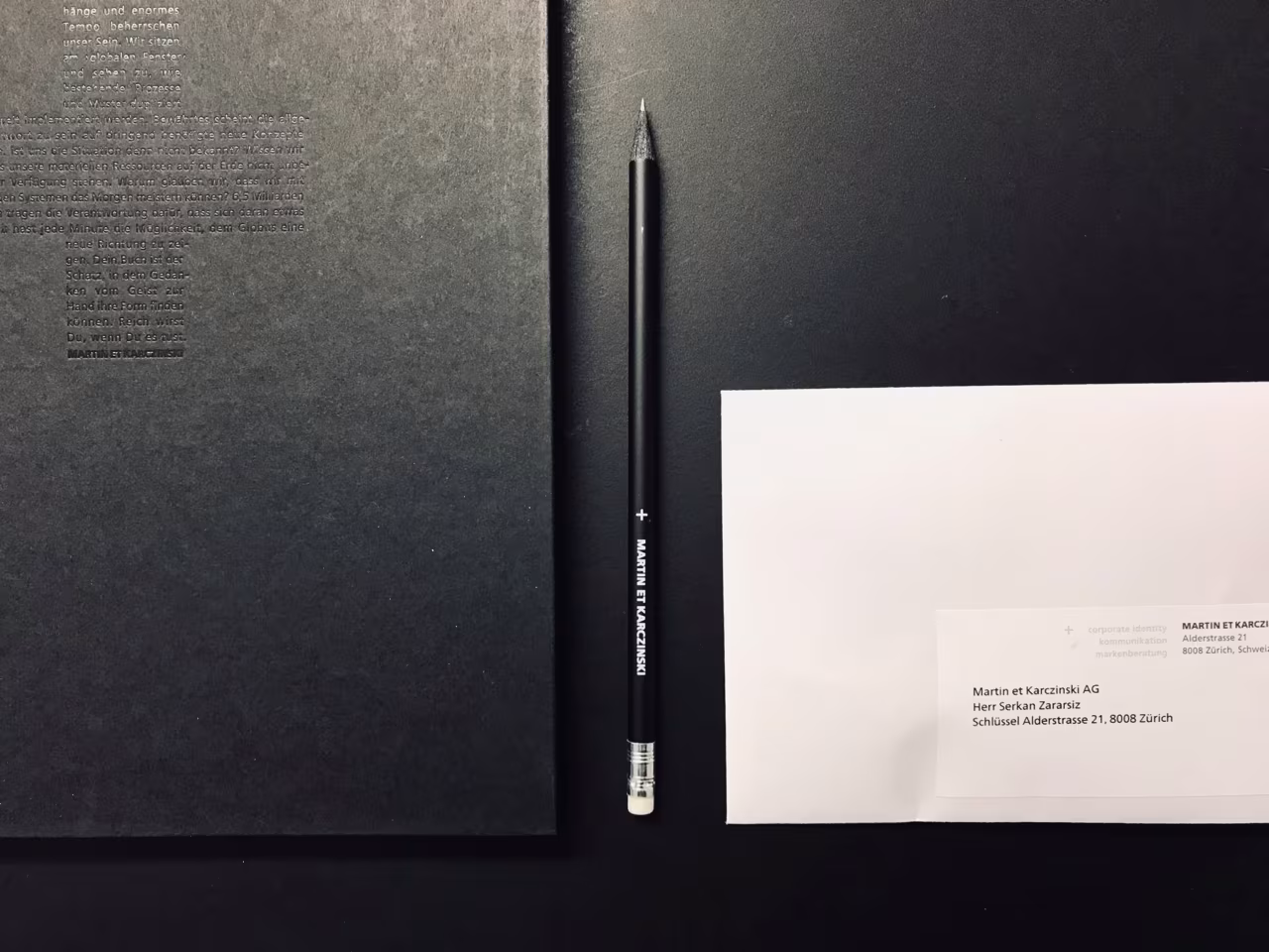 Welcome package on a black desk: a black notebook, a pencil with the agency's name and a welcome letter